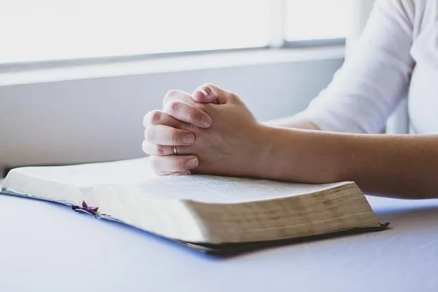 Mãos unidas em oração sobre uma Bíblia aberta