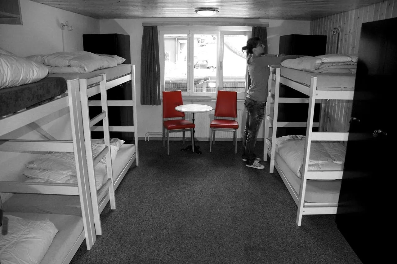 Quarto de hostel com beliches e mesa com cadeiras vermelhas