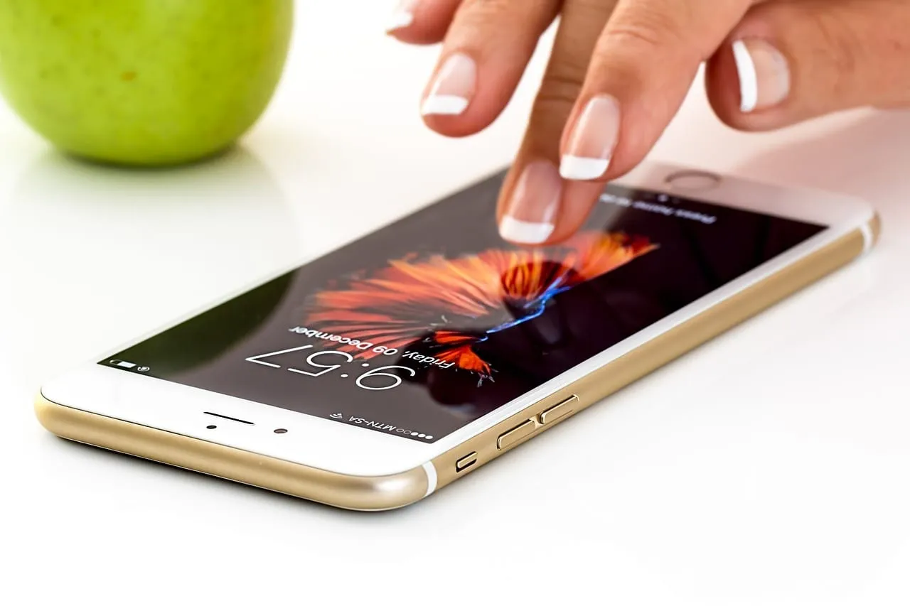 Dedo tocando a tela de um iPhone dourado ao lado de uma maçã verde